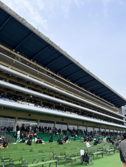 Multi-tiered concrete grandstand at Let’s Run Park Seoul viewed from outside, with green painted seating tiers and outdoor benches occupied by visitors on a clear day