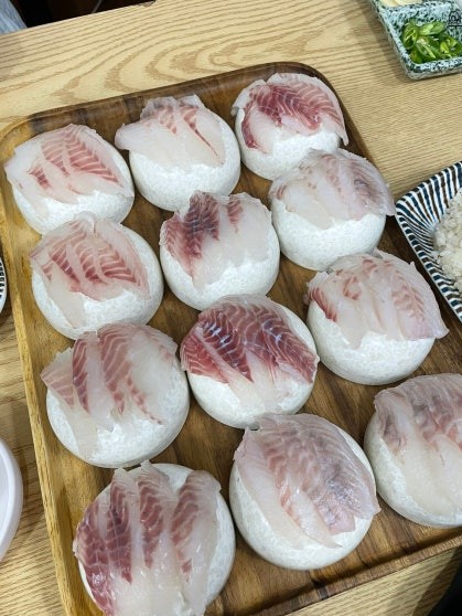 Twelve portions of raw black sea bream sashimi arranged over mounds of steamed white rice on a rectangular wooden serving tray, side dish of seasoned rice visible at the back corner