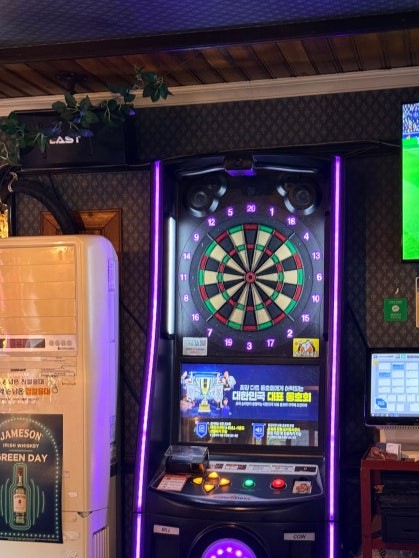 Electronic dart machine with purple LED lights at Rose & Crown Itaewon, with a sports broadcast screen and Jameson whisky signage visible behind