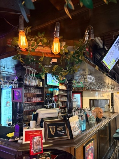 Dark wood bar counter at Rose & Crown Itaewon with Edison bulb pendant lights, trailing vine decoration, and wine glasses hanging overhead